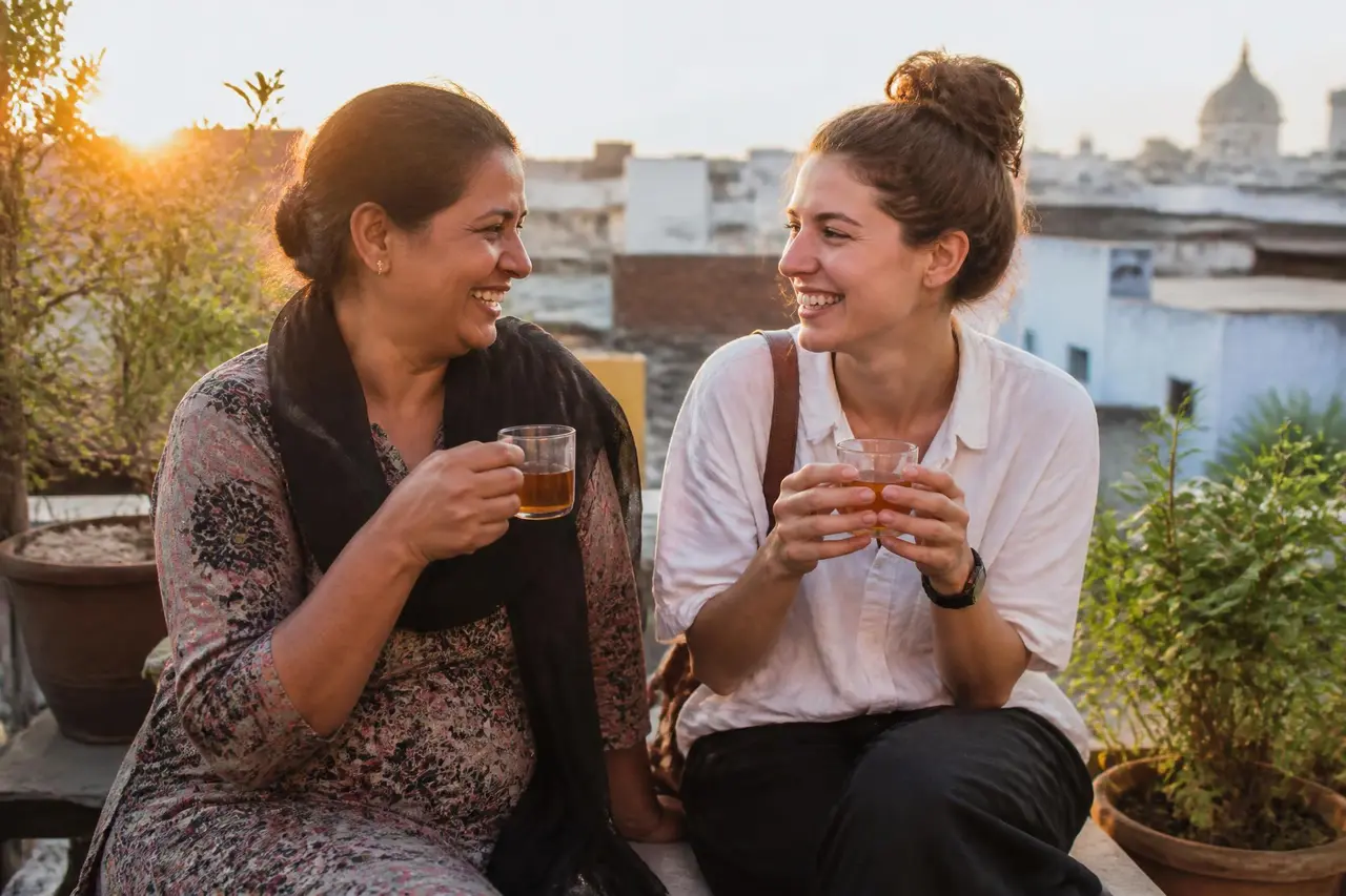 A local host and a traveler laughing together over tea on a rooftop at sunset